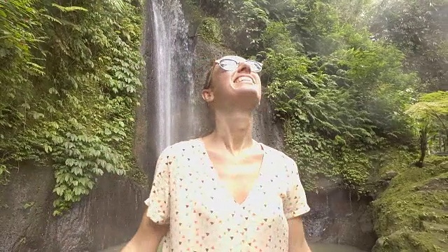 慢动作年轻女子享受新鲜瀑布在巴厘岛，印度尼西亚，亚洲。人们旅游乐趣自然的概念。女孩伸着胳膊视频下载