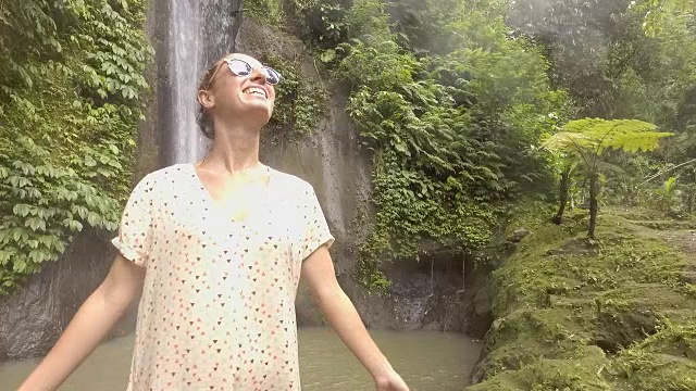 年轻女子在巴厘岛的瀑布上凝视大自然，享受大自然的新鲜。人们出行绿色环保理念。慢动作拍摄视频下载