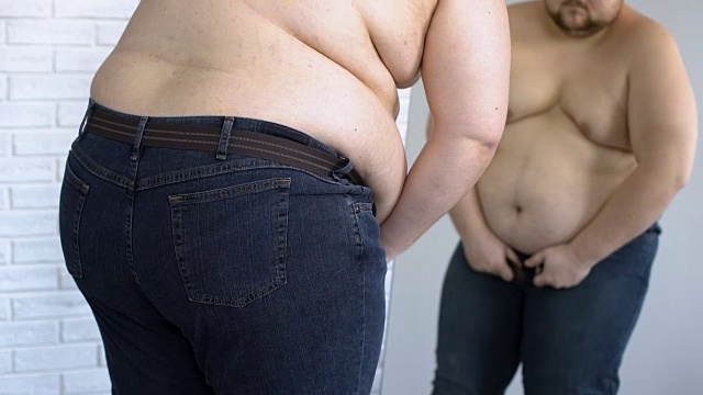 试图穿紧身牛仔裤的肥胖男性，超重问题，不健康的生活方式视频素材