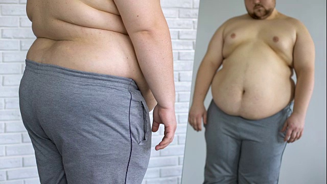 伤心超重的男人看着胖胖的肚子镜子反射，减肥的问题视频素材