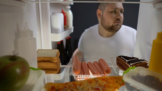 上瘾的年轻人晚上在冰箱附近吃香肠，不健康营养视频下载