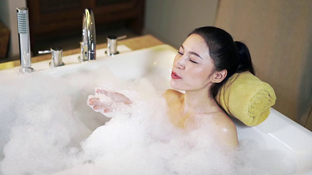 一个女人在浴缸里泡澡，吹肥皂泡的慢动作视频下载