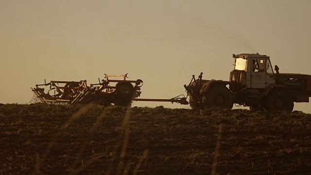日落农民的剪影在拖拉机俄罗斯农业土壤地面准备土地与苗床中耕机作为提前播种活动的一部分在早春季节的生活方式农业工作在农田视频素材