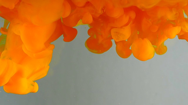 墨水在水里。橙色闪光涂料与水反应形成抽象的云。可以用作过渡，添加到现代垃圾项目，艺术背景，任何创造性扭曲视频素材