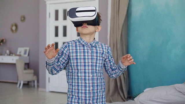 可爱的小男孩试着戴虚拟现实眼镜，站在他的公寓里打手势。现代科技、娱乐与人的观念。视频素材