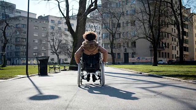 残疾的小女孩坐在城市公园的轮椅上视频素材