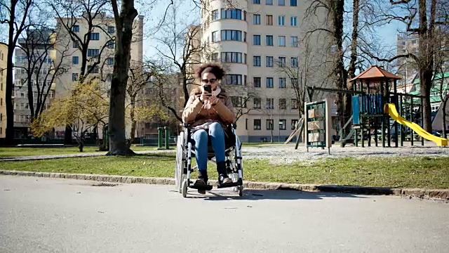 残疾的小女孩坐在城市公园的轮椅上视频素材