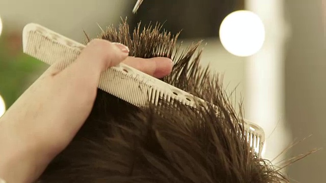 手发型师用剪刀剪头发并仔细梳理。理发师在美容院用专业剪刀和梳子制作男性发型视频下载
