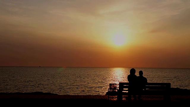 男人和女人坐在长椅上看海上的日落视频下载