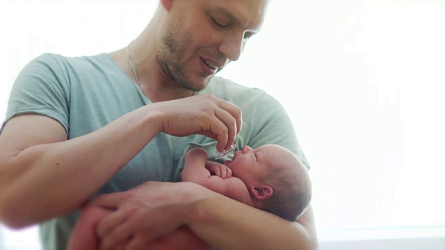 一位年轻的父亲用奶嘴安抚新生儿。孩子把奶嘴放进嘴里吮吸。新生儿学。父亲节。儿童节视频素材