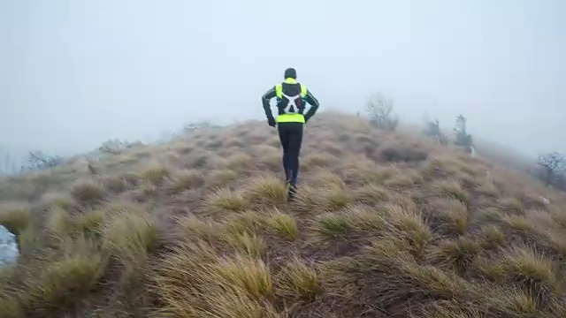 在一个寒冷的早晨，跑步者在他的油炸食品后面跑过雾蒙蒙的山视频下载