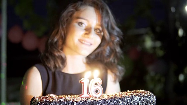 快乐的少女在16岁生日派对上拿着蛋糕和燃烧的蜡烛微笑和有乐趣，手持拍摄视频素材