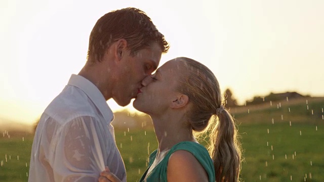 镜头光晕:美丽的金发女人和英俊的男人在夏日的雨中接吻。视频素材