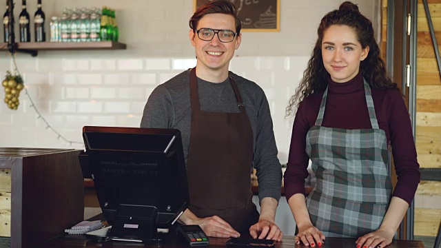 两个年轻英俊的服务员站在收银台在咖啡厅微笑的肖像。成功的生意，快乐的人和餐饮的服务理念。视频素材