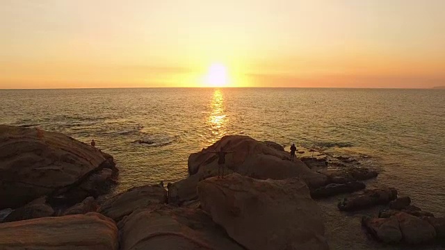 鸟瞰图，剪影男子在岩石顶部与手臂举起在日落的海滩视频素材