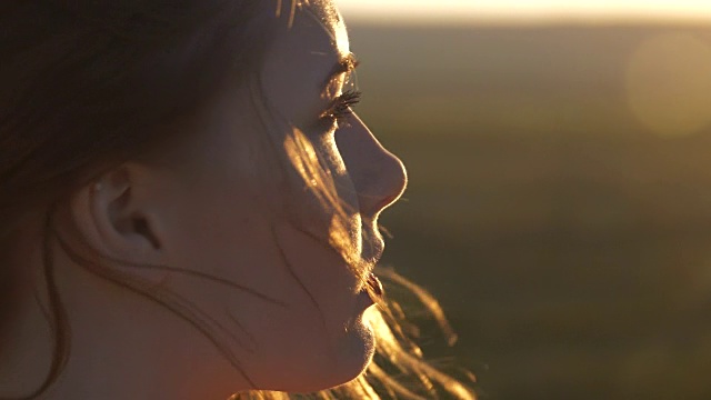 一个年轻美丽的女人看着夕阳的脸风吹动了她的头发视频素材
