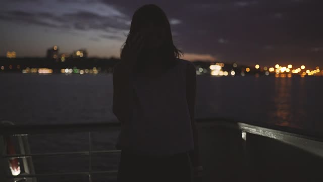 一个年轻迷人的女人的剪影，背景是夜城上的一艘船视频素材