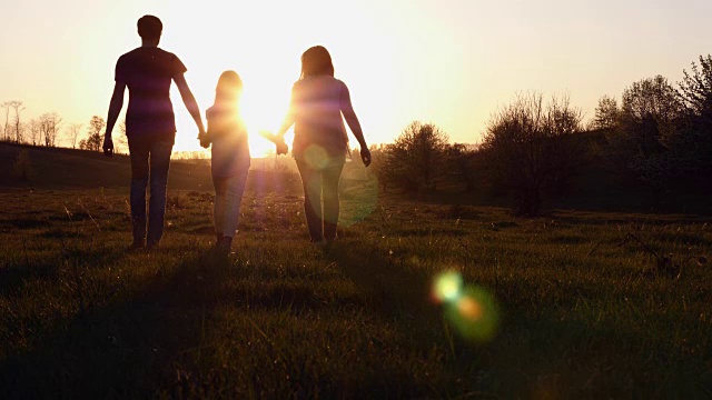 夕阳下父亲和母亲带着女儿散步的剪影视频素材