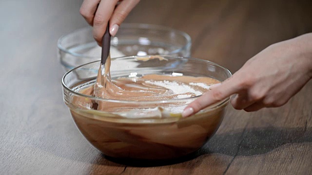 糕点师在煮生面团。一只手用塑料抹刀在一个碗里搅拌面团，烤一个巧克力饼干蛋糕。视频素材