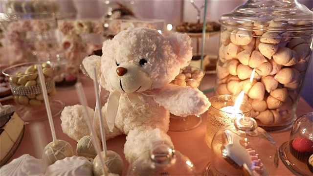 糖果棒在餐厅，孩子们的聚会，生日，一个白色的泰迪熊的脖子上有一只蝴蝶，点燃蜡烛，泰迪熊在桌子上的糖果棒视频下载
