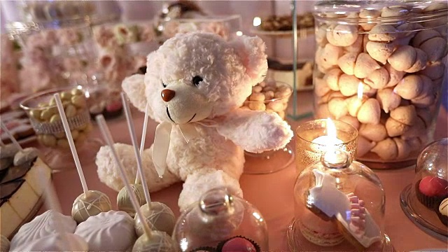 糖果棒在餐厅，孩子们的聚会，生日，一个白色的泰迪熊的脖子上有一只蝴蝶，点燃了蜡烛，泰迪熊在桌子上的糖果棒，特写视频下载
