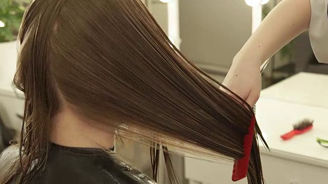 手理发师在美发厅为女士理发时梳理长发。近距离观察美发师在美容院为女性理发视频下载