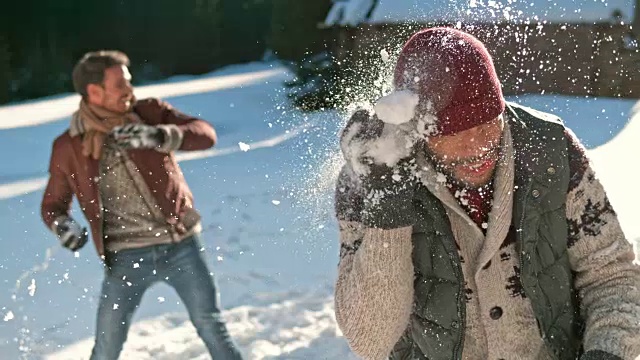 一个阳光明媚的日子，一个年轻人在外面的雪地里被雪球击中视频素材