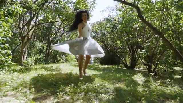 一个穿着蓝色裙子的漂亮的黑发女人跑过花园，慢镜头视频下载