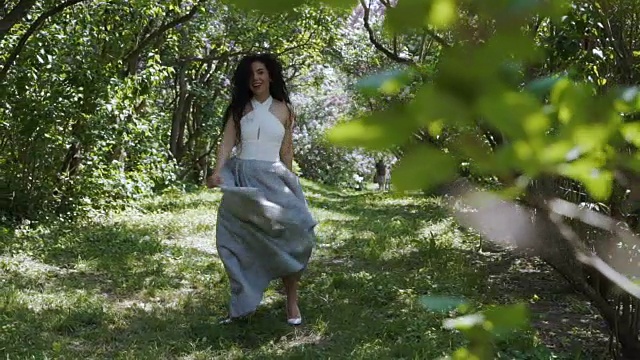 迷人的黑发女郎移动她的长连衣裙站在绿色的花园视频下载