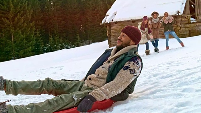 SLO MO Man在推着他笑着的朋友坐雪橇下山时摔倒在地视频素材