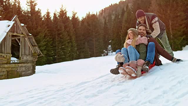 一男一女坐在雪橇上，被一个男性朋友推下山坡视频素材