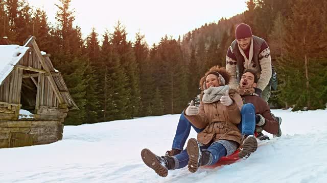 一名男子和一名女子坐在雪橇上，被一名男性朋友推下山坡视频素材