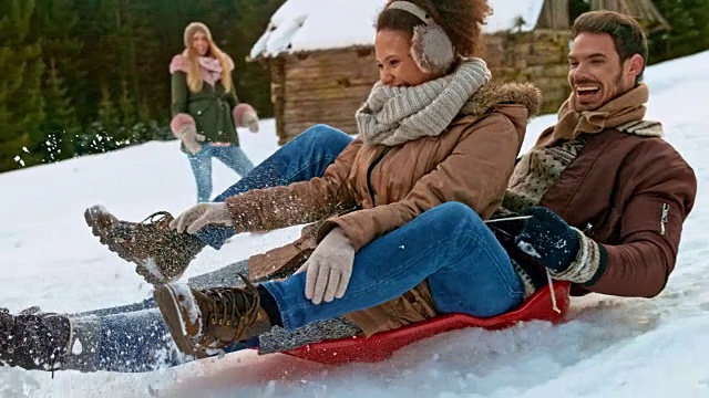 一名男子和一名女子坐在雪橇上，被一名男性朋友推下山坡视频素材