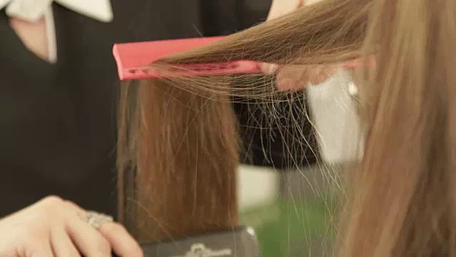 发型师在美容院为时装模特使用发夹和梳子拉直头发。近距离的理发师直发在美发沙龙的女人造型视频下载