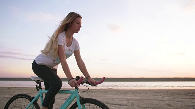 年轻迷人的女子骑着自行车在海边的海滩上，在日出或日落，慢镜头视频素材