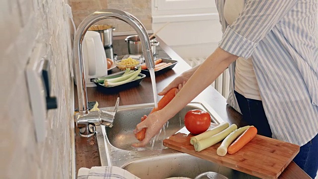 一个面目全非的女人在厨房做饭的时候洗蔬菜。视频素材