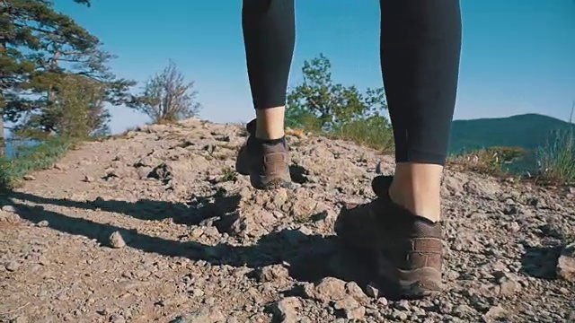 在山崖上徒步旅行的女旅行者的脚上的观点。慢动作视频素材