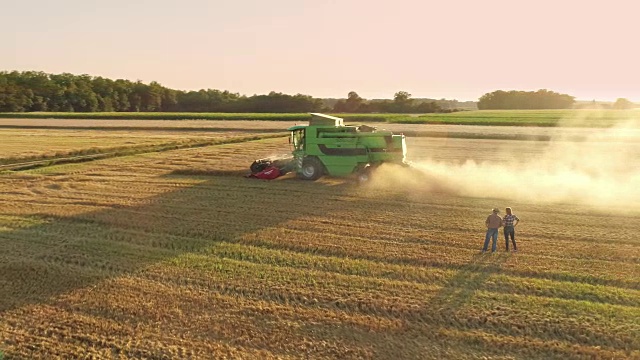 无人机视角的农民看着联合收割机收获阳光，农村小麦作物，慢镜头视频素材
