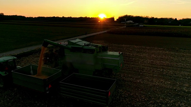 无人机视角联合收割机斜槽填充拖车与收获的玉米在日落，慢镜头视频素材
