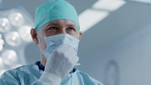 成功手术后专业外科医生摘下外科口罩的肖像。现代医院手术室的背景。视频素材