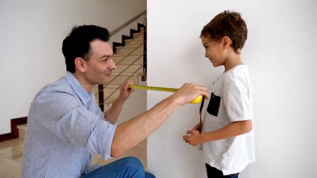 慈爱的父亲教他的儿子如何测量一堵墙指导他，看起来很自豪视频下载