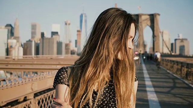 美丽的白人女孩享受温暖阳光明媚的天气，回头看镜头微笑在布鲁克林大桥4K视频素材