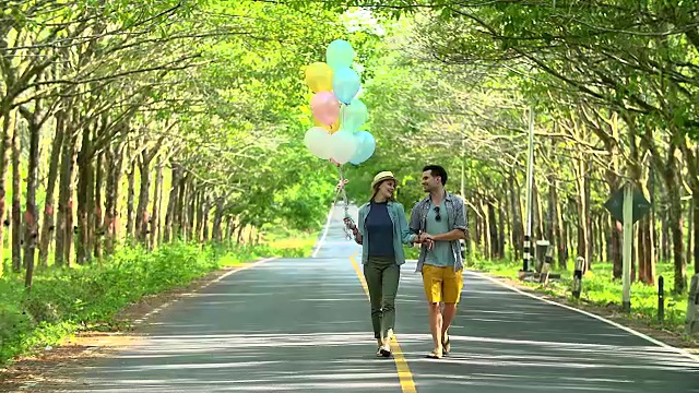 一对年轻幸福的夫妇带着气球一起走在路上。视频素材