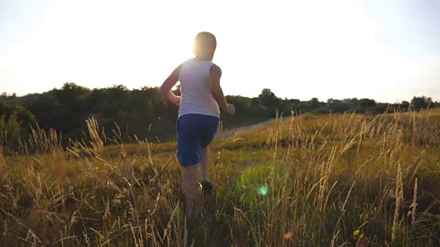 在阳光明媚的一天，一个小男孩在草地上跑步。孩子在草坪上慢跑，脸上还带着太阳耀斑。在夏日草地上，男孩在大自然中休息。慢动作特写后视图视频素材