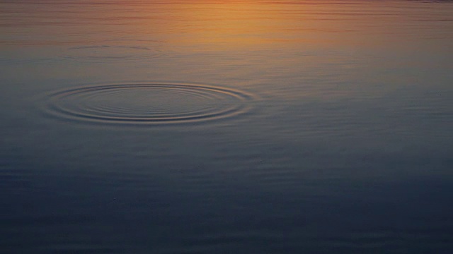 石头在平静的水面上跳跃，美丽的夕阳围绕。视频下载