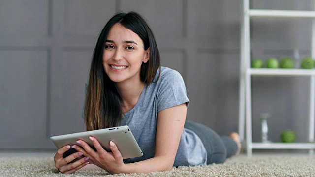 年轻快乐的女人躺在地板上，摆着平板电脑的姿势视频下载