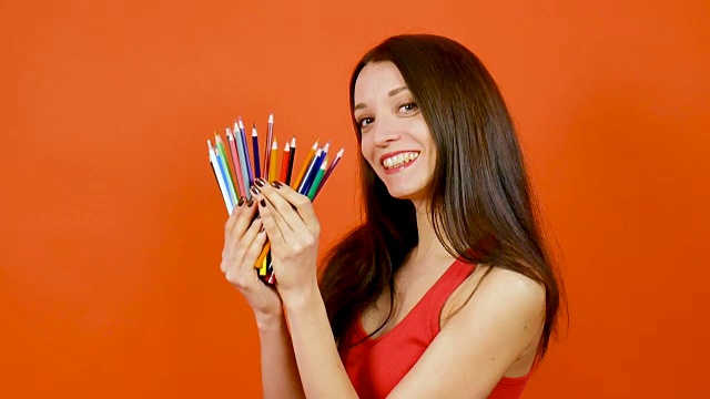年轻的黑发女人与彩色铅笔摆姿势在一个橙色的背景。艺术设计的概念视频下载