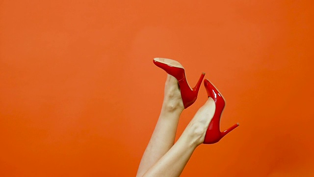 性感女人的腿在明亮的橙色背景红色高跟鞋。它们从一边摇到另一边。红专利鞋。慢动作视频下载