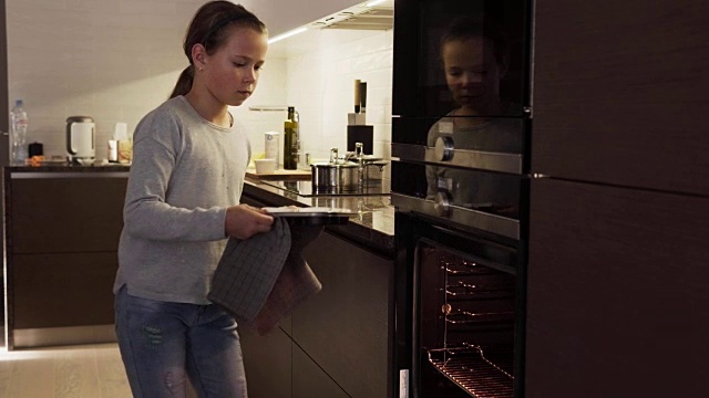 在现代化的厨房里，女孩把饼干放进烤箱烤视频素材