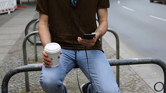年轻男子在街道的栏杆上使用智能手机视频素材